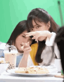 two girls are sitting at a table with a plate of pizza and a cup of bubble tea .