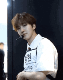 a young man wearing a white shirt and tie is holding a microphone in his mouth and looking at the camera .