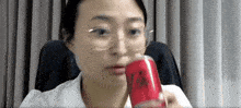 a woman wearing glasses is holding a can of soda in her hand .