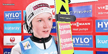 a woman stands in front of a wall with advertisements for hylo and kronen zeitung