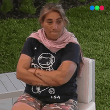 a woman wearing a shirt that says isa sits on a couch with her arms crossed