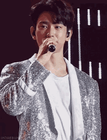 a young man is singing into a microphone while wearing a sequined jacket .