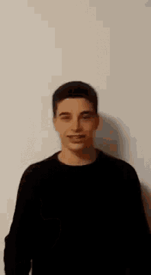 a young man wearing a black sweater is smiling and giving a peace sign
