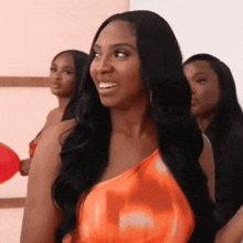 a woman with long black hair is wearing an orange one shoulder top