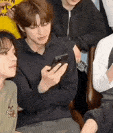 a young man is sitting in a chair holding a cell phone in his hand .