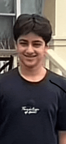 a young man wearing a blue shirt is smiling and standing in front of a building .