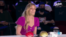 a woman in a purple top is sitting at a table with a deluxe logo on the bottom