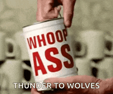 a person is holding a can of whoop ass thunder to wolves .