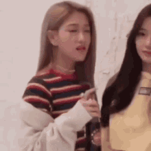 two young women are standing next to each other in a room . one of the girls is wearing a striped shirt .