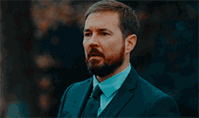 a man with a beard is wearing a blue suit and tie