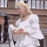 a woman in a white dress and a hat is standing next to another woman in a white dress .