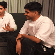 two men are sitting on a couch and one has a white t-shirt that says tnt on it