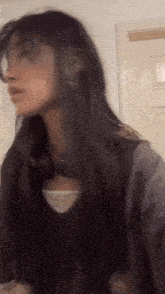 a woman with long black hair is standing in front of a door and looking at the camera .