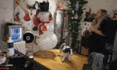 a woman stands in front of a christmas tree and a snowman in a living room