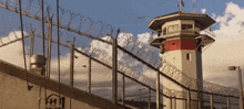 a barbed wire fence surrounds a prison tower with a flag on top
