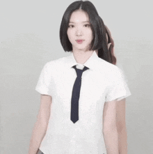 a young woman in a school uniform and tie is standing in front of a white wall .