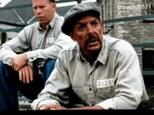 two men are sitting on a bench and one has a tag on his shirt that says 3026