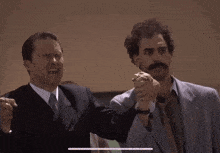 two men in suits and ties are holding hands