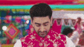 a man is wearing a red vest with gold embroidery on it .