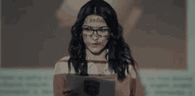 a woman wearing glasses is holding a piece of paper in front of a screen .
