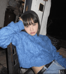 a woman wearing a blue sweater is leaning against a wall