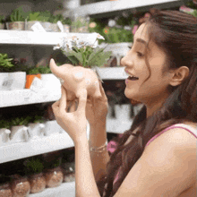 a woman in a pink tank top is holding a potted plant in her hand