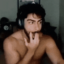a shirtless man with a beard wearing headphones is sitting in a room .