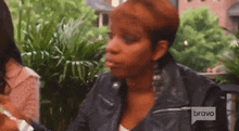 a woman in a leather jacket is sitting at a table with a bravo logo on the bottom of her jacket .