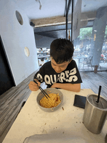 a boy wearing a black shirt that says quares is eating noodles with chopsticks