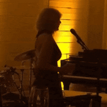 a woman singing into a microphone in front of a piano and drums