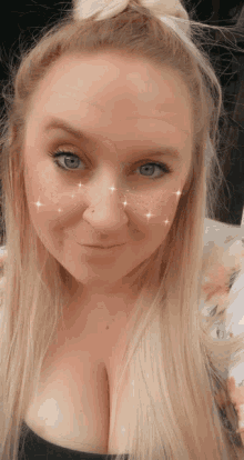 a woman with blonde hair and blue eyes is smiling with sparkles on her face