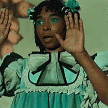 a girl with green eye shadow and a flower in her hair holds her hand up
