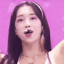 a close up of a woman 's face with a purple background . she is wearing a headband and necklace .