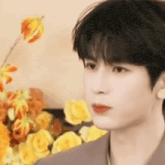 a close up of a young man standing in front of a bouquet of yellow flowers .