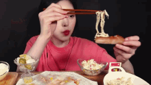 a woman in a pink shirt is eating a sandwich with chopsticks .