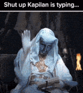 a man in a white robe is sitting in front of a fire with the words shut up kapilan is typing
