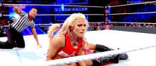 a woman is laying on the ground in a wrestling ring with a referee kneeling behind her .