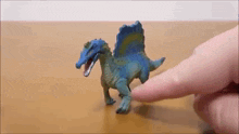 a toy dinosaur is being touched by a person 's finger on a wooden table .