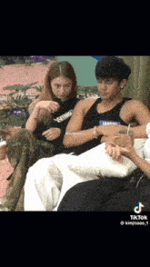 a man and a woman are sitting on a couch and the man is wearing a tank top that says sydney