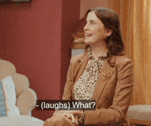a woman in a brown suit laughs while sitting in a chair