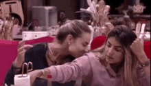 two women are sitting next to each other on a couch and kissing each other .