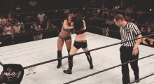 two women wrestling in a wrestling ring with a referee watching