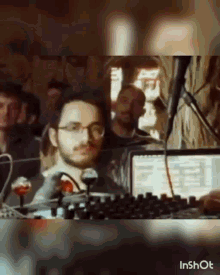 a man with glasses and a beard is sitting in front of a laptop computer .