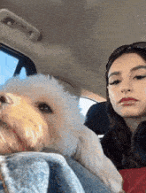 a woman sitting in a car with a small white dog on her lap