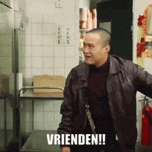 a man in a brown jacket is standing in a kitchen with the word vrienden written on the floor