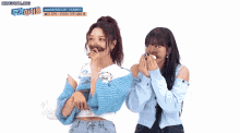 two women are standing next to each other with their hands over their mouths .