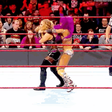 two women are wrestling in a ring with a crowd watching . one of the women is wearing a purple outfit .