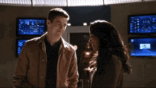 a man and a woman are standing next to each other in a room with a lot of monitors on the wall .