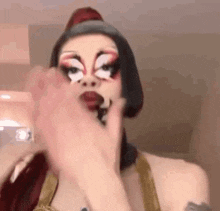a drag queen is applying makeup to her face and making a funny face .