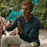 a man in a blue shirt is sitting on a beach